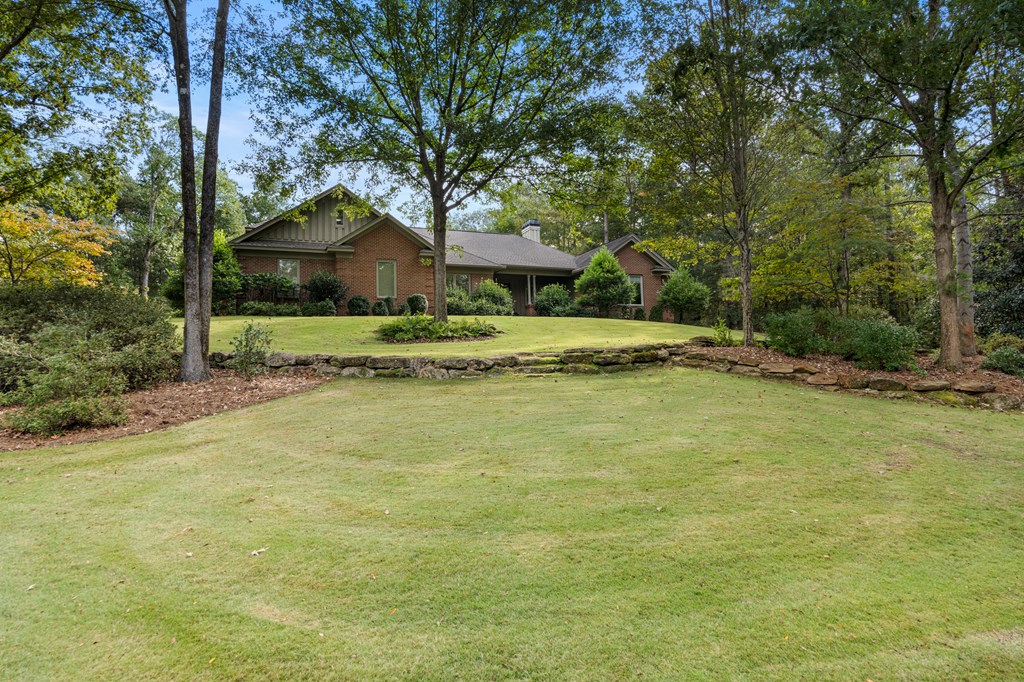 Brick ranch home set behind a broad lawn and low stone retaining wall.