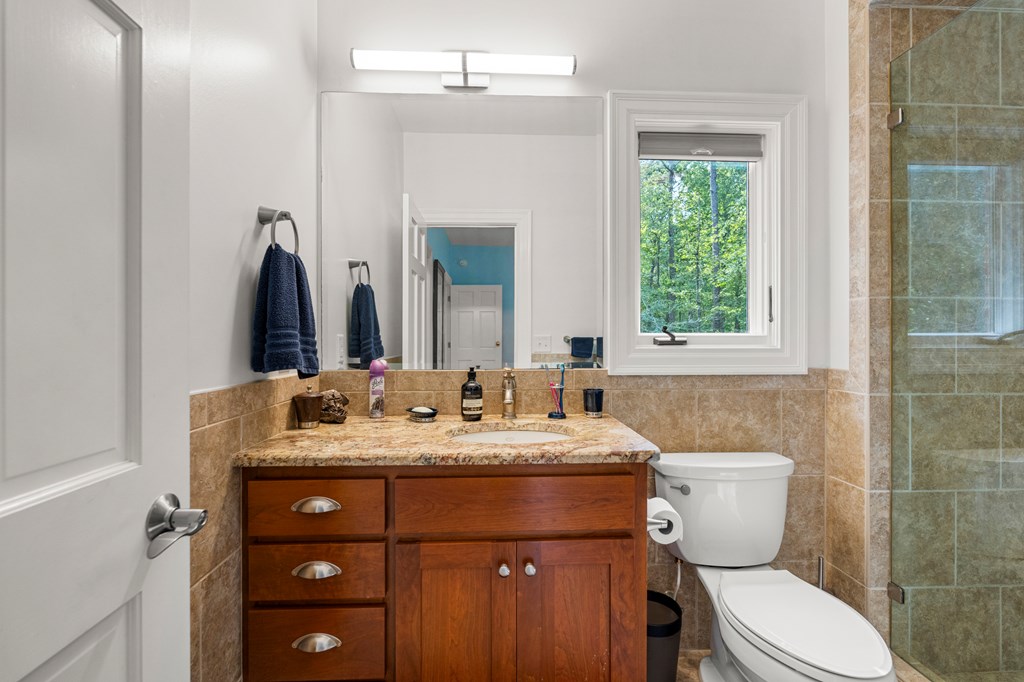 Bathroom with a wooden vanity, stone countertop, and window overlooking trees.