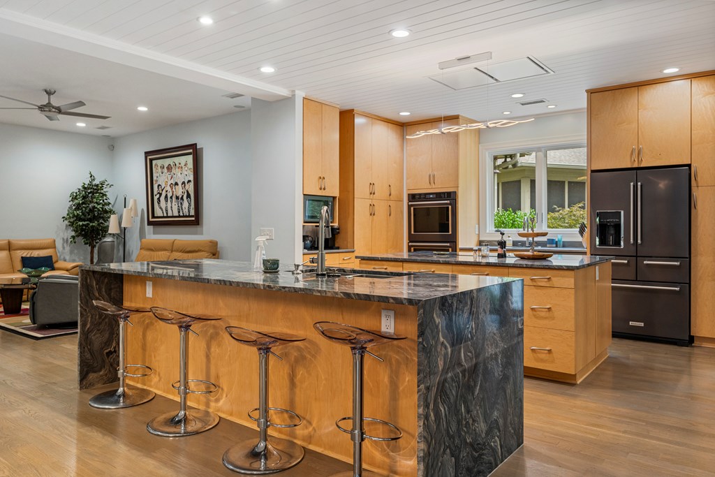 Kitchen with a large dark stone island, bar stools, wood cabinets, and stainless steel appliances.