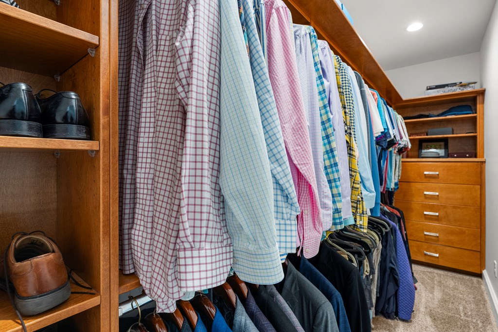 Walk-in closet with wood shelving, organized shirts and trousers, and built-in drawers.