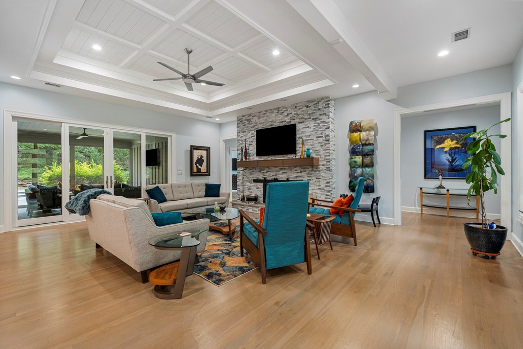 Furnished living room with a stone fireplace, coffered ceiling, and sliding glass doors to greenery.