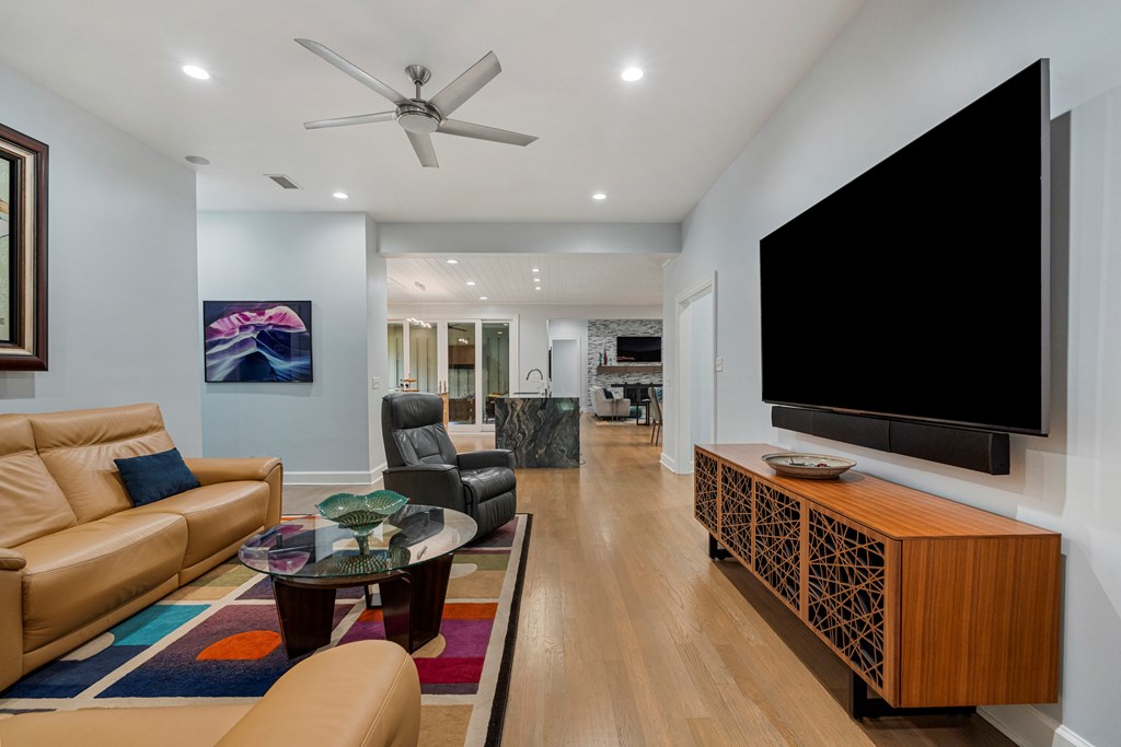 Living room with tan leather sofas, a colorful rug, and a large wall-mounted television.