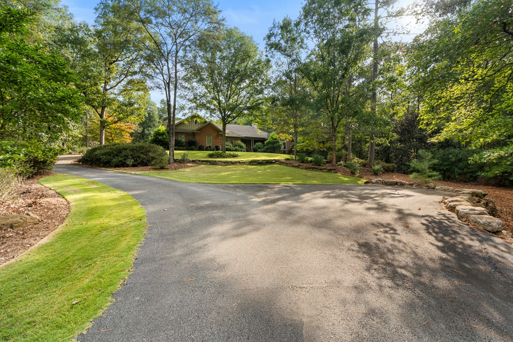 Brick home among mature trees beyond a curving driveway and lawn.
