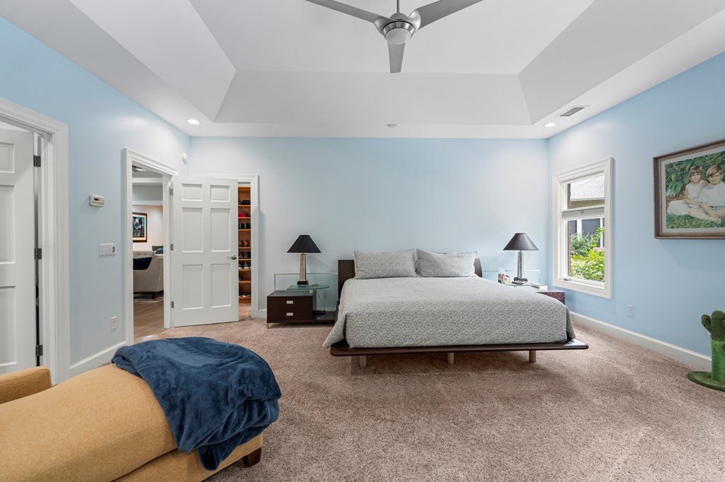 Furnished bedroom with a large bed beneath a tray ceiling and ceiling fan.