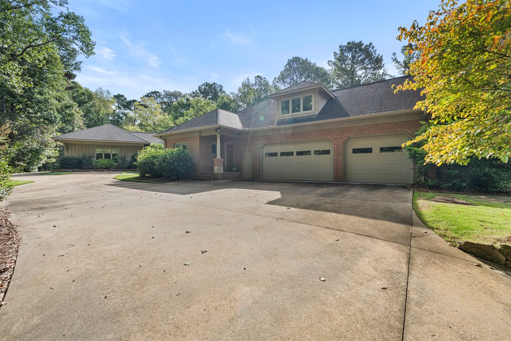 Brick home with two attached garage doors, a broad concrete driveway, and mature trees.