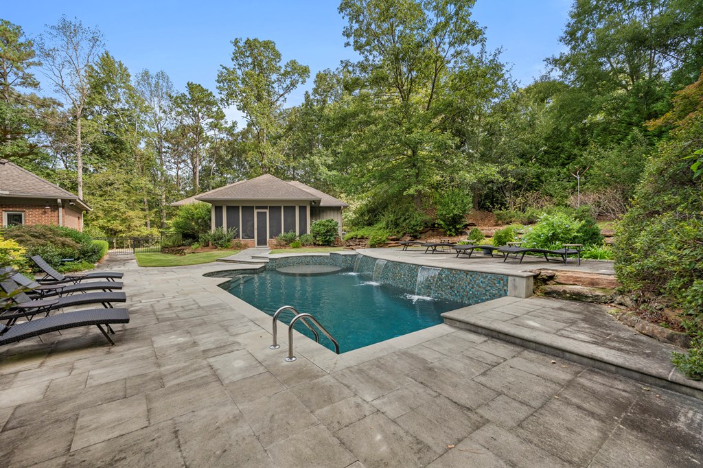 Outdoor pool with a screened pool house, lounge chairs, and a stone-paved patio.