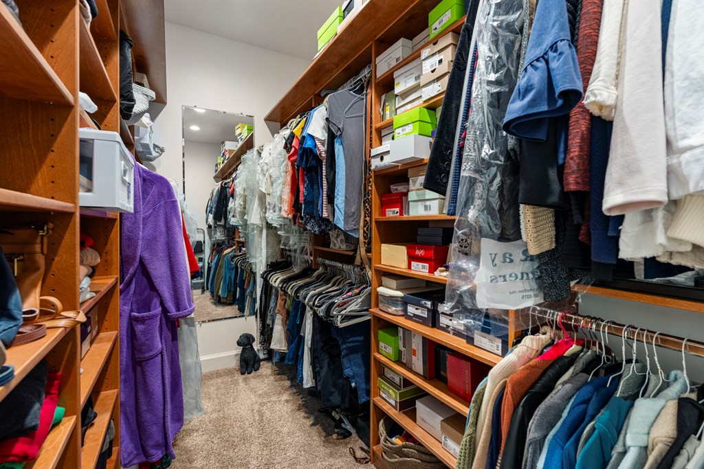 Walk-in closet with built-in wooden shelves, hanging clothes, and shoe boxes.