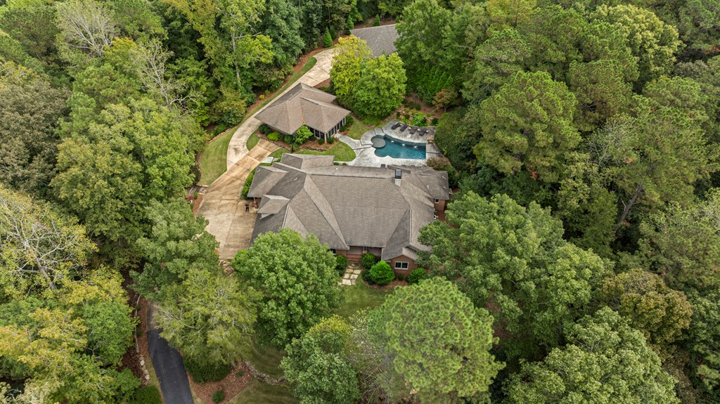 Aerial view of a brick home and swimming pool surrounded by dense trees.