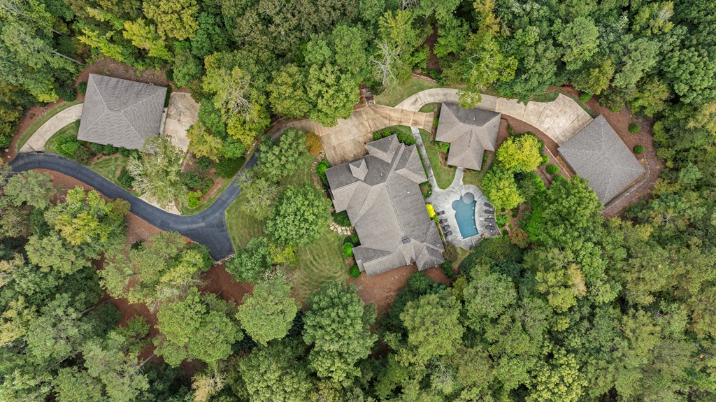 Aerial view of a wooded property with a swimming pool and several detached structures.