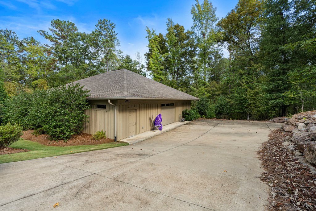 Detached beige garage beside a wide concrete driveway, surrounded by mature trees.