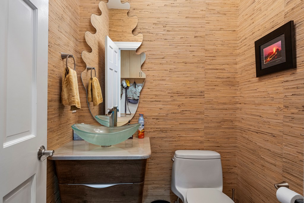 Bathroom with bamboo paneling, a green glass vessel sink, and an irregular wood-framed mirror.