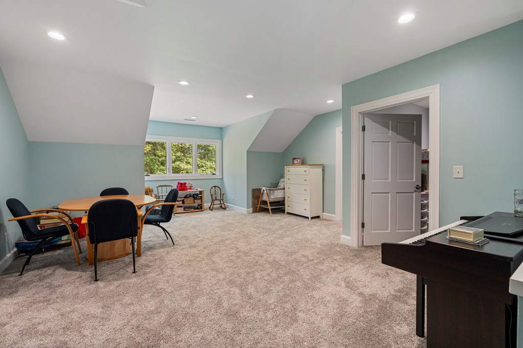 Finished bonus room with sloped ceilings, beige carpet, a round table, and an electronic keyboard.