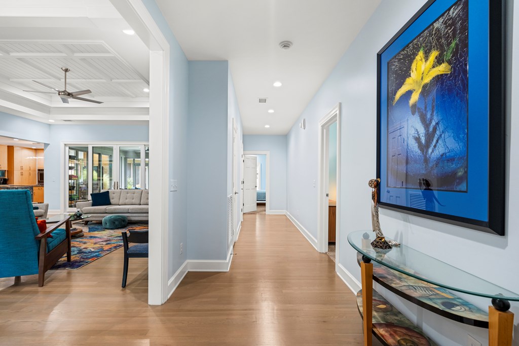 Hallway opening to a living room, with light wood floors and large blue-framed floral artwork.