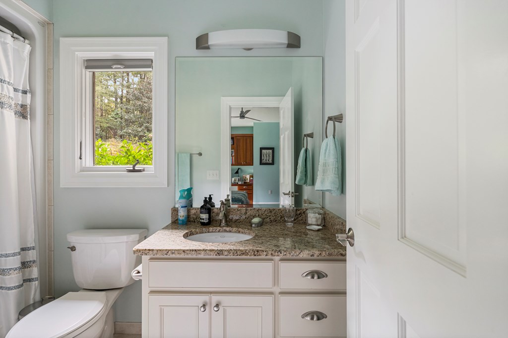 Bathroom with granite-topped white vanity, large mirror, and a window beside the shower.