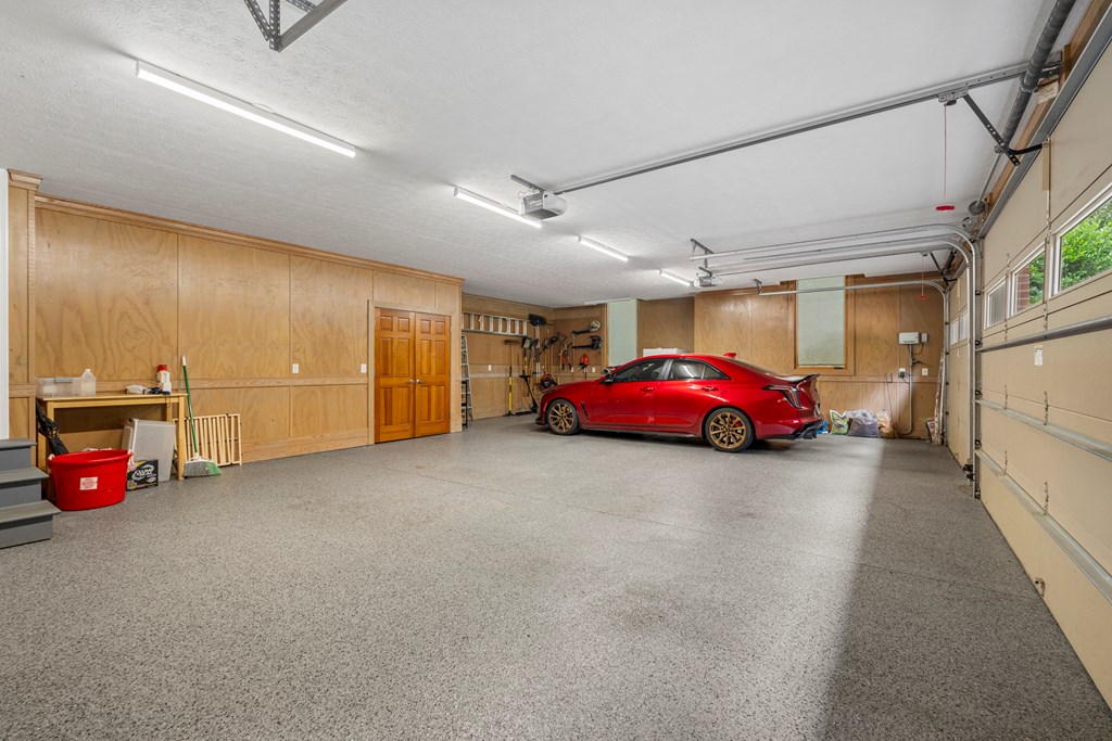 Spacious garage with speckled flooring, wood-paneled walls, and a red car.