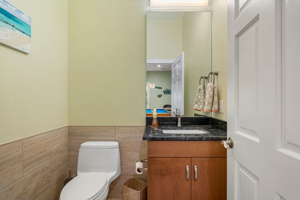 Bathroom with a wood vanity, dark stone counter, and beige tile wainscoting.