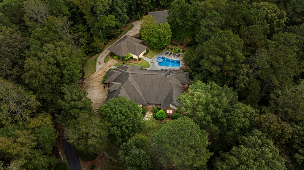 Aerial view of a wooded home with a curved driveway and backyard pool.