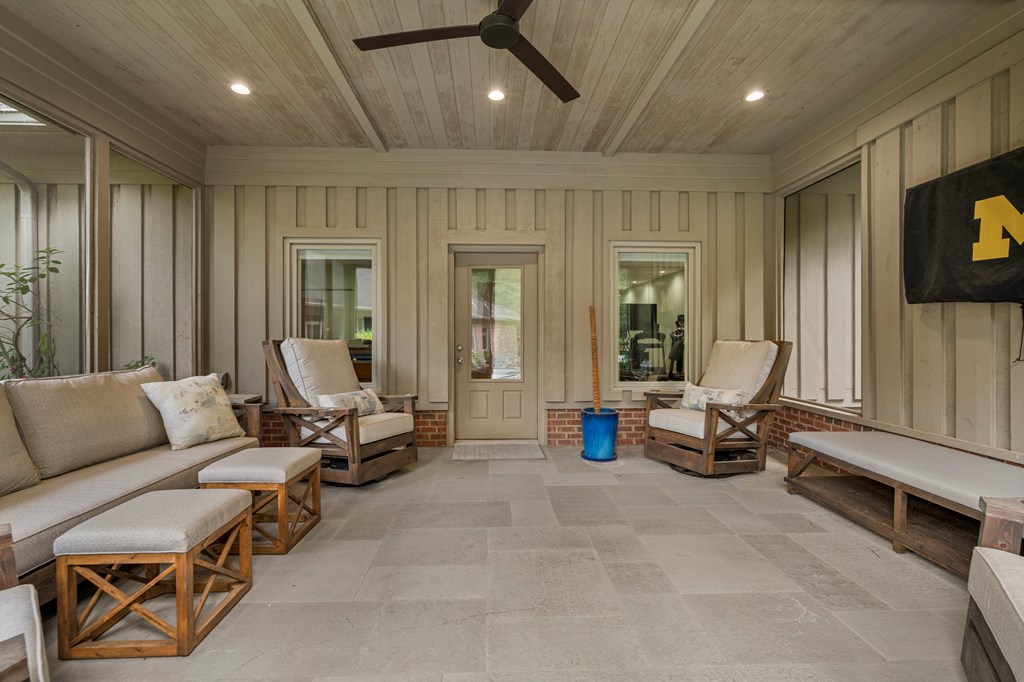 Sunroom with cushioned wood seating, a plank ceiling, paneled walls, and large gray floor tiles.