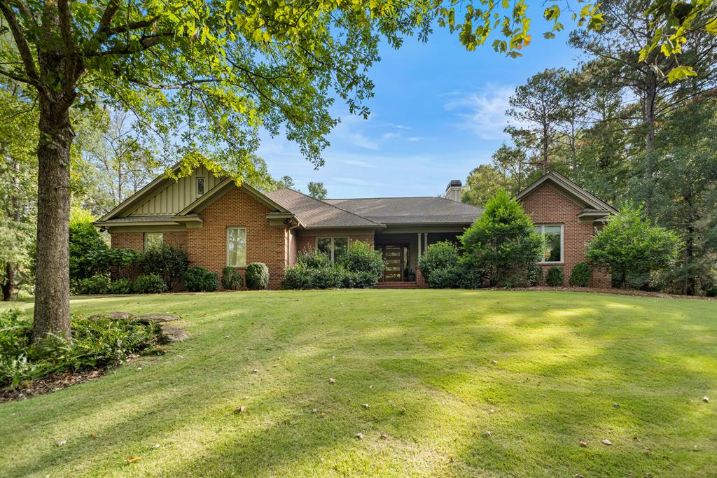 Single-story brick home with a covered entry, mature trees, and a broad front lawn.