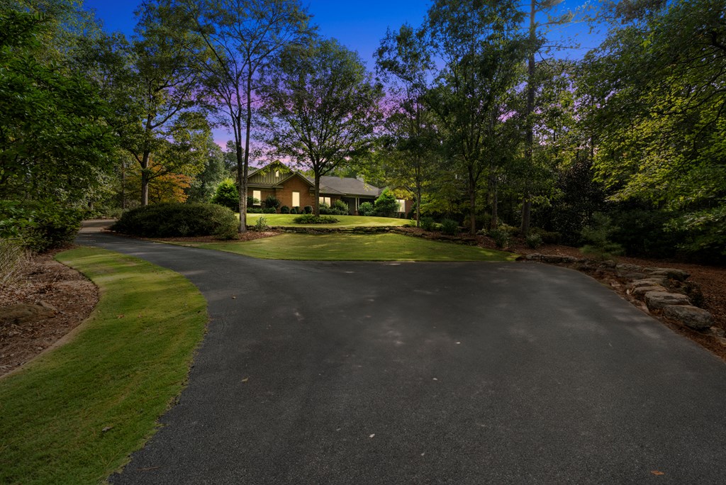 Brick home set among mature trees, with a broad curved driveway and landscaped front lawn.