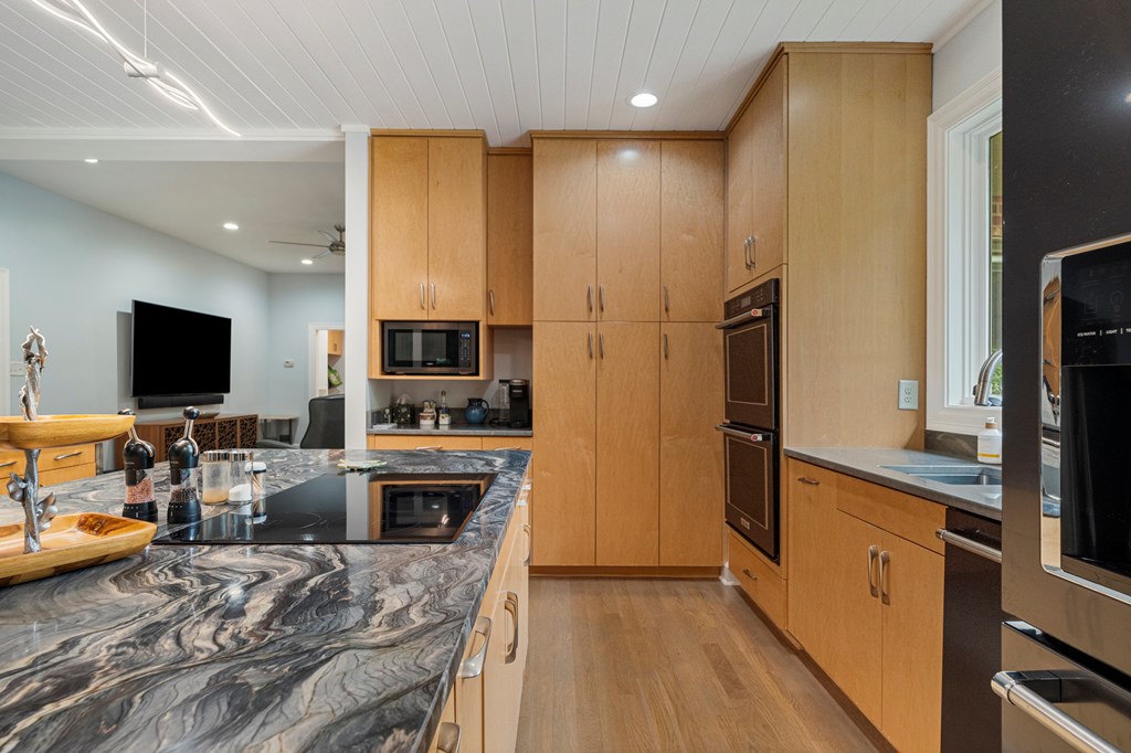 Kitchen with warm wood cabinets, double ovens, and a marble-patterned island with a cooktop.