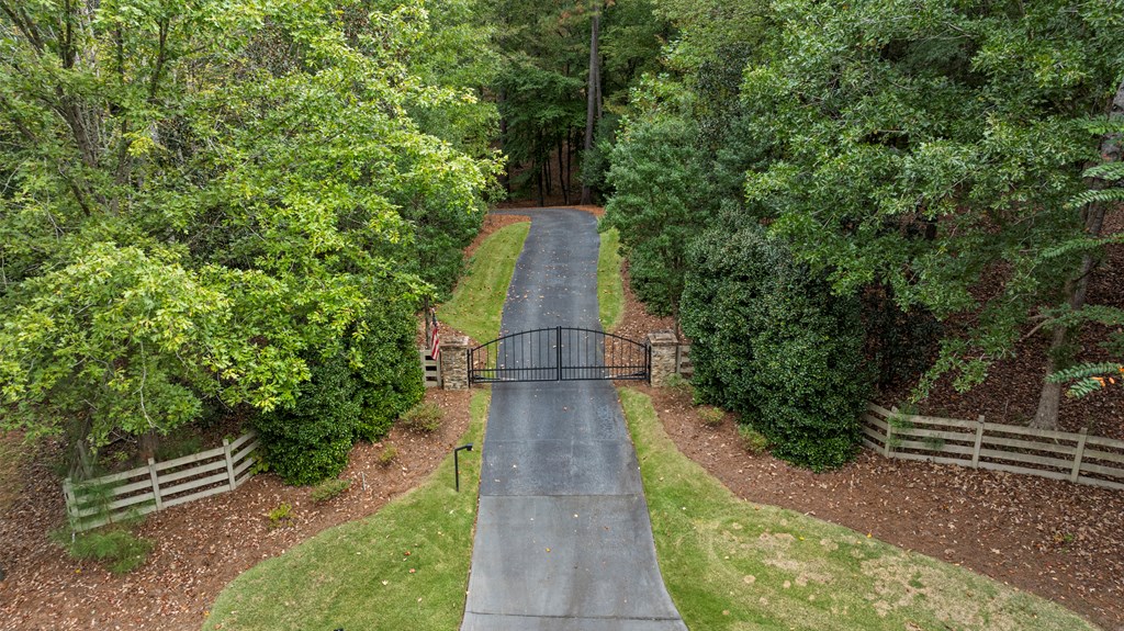 Paved driveway entrance with a black metal gate, stone pillars, and wooded landscaping.