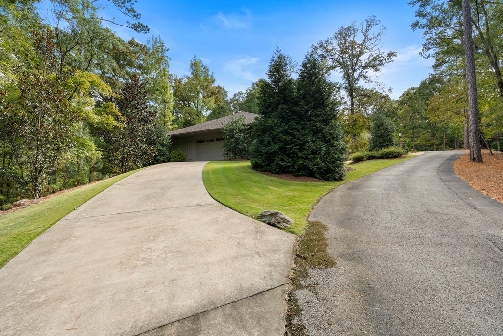 Home among mature trees, with a curved driveway leading to a partly obscured garage.