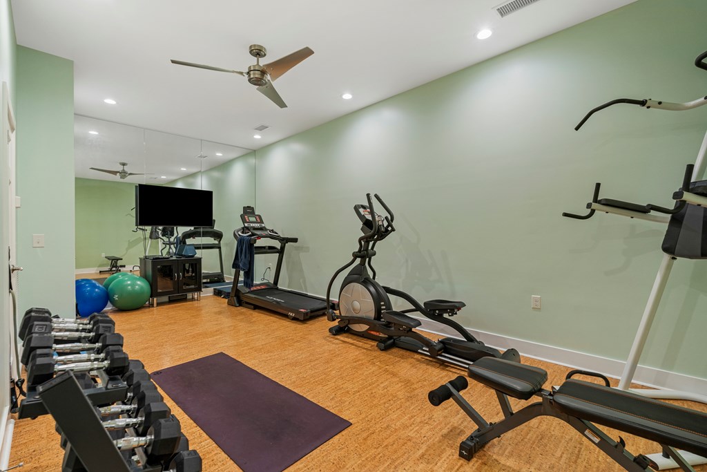 Home gym with mirrored wall, wood flooring, dumbbells, treadmill, and elliptical machine.