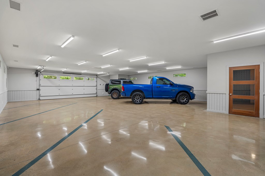 Spacious garage with a polished concrete floor, blue markings, and two pickup trucks.