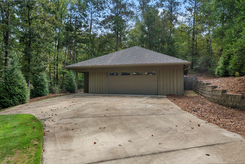 Detached garage with a wide door and concrete driveway, surrounded by mature trees.