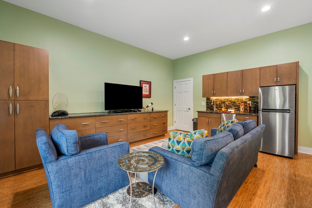 Living room with blue sofas, extensive wood cabinetry, and a stainless steel refrigerator.