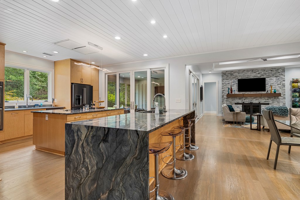 Open-plan kitchen with a large veined stone island and adjoining living area with a stone fireplace.