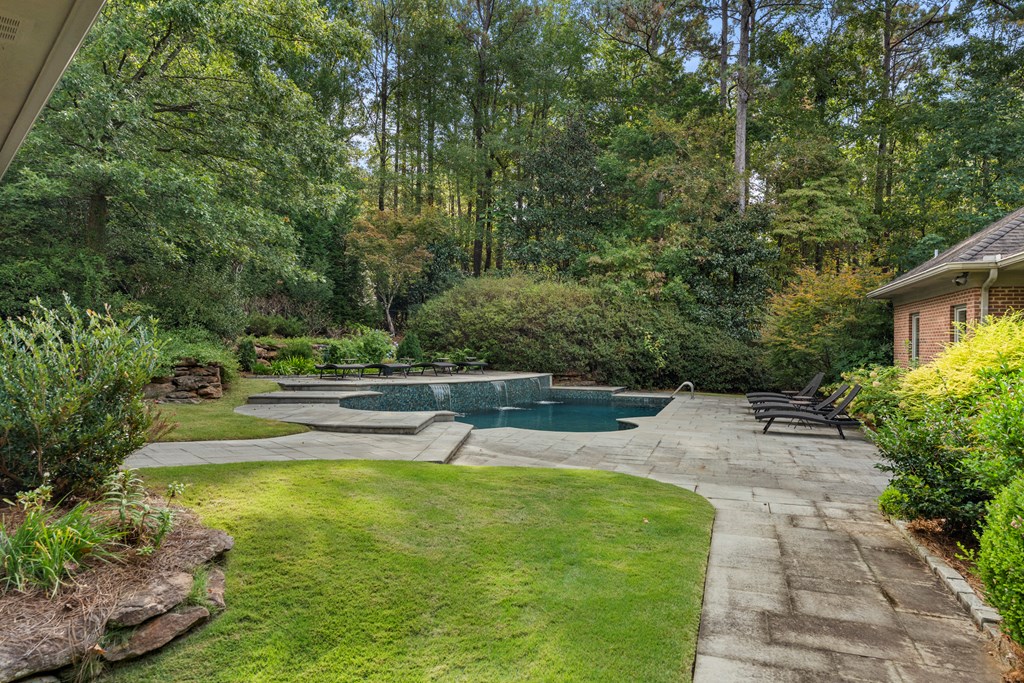 Backyard pool with a raised spillover section, stone patio, lounge chairs, and wooded landscaping.