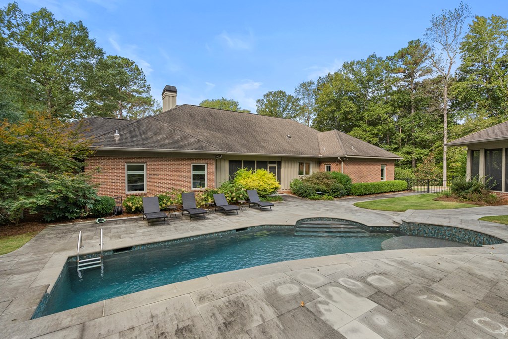 Back of a brick home with a swimming pool, paved patio, and lounge chairs.