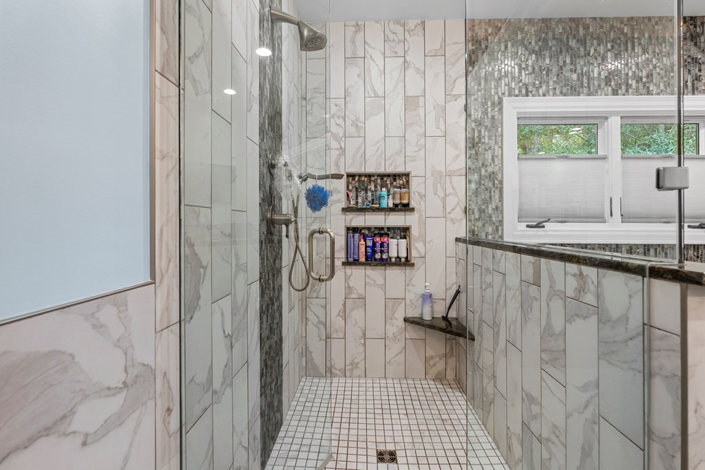 Walk-in shower with marble-look tile, built-in niches, glass enclosure, and a window.