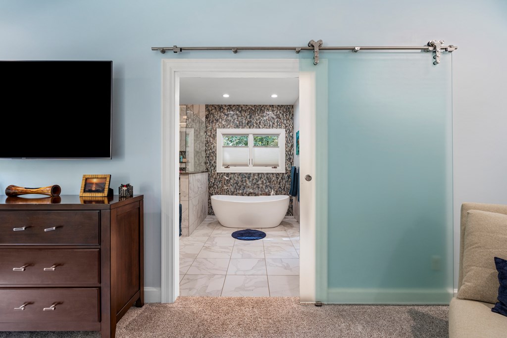 Bathroom with a freestanding tub beneath a window, mosaic tile walls, and a sliding frosted-glass door.