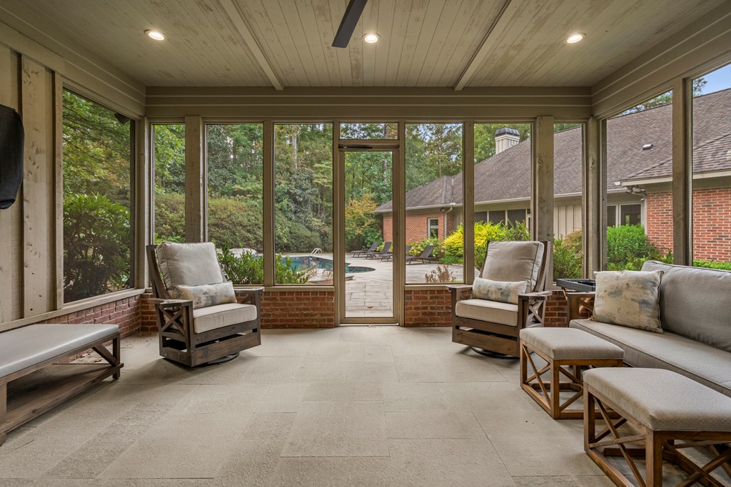 Furnished sunroom with broad windows overlooking a swimming pool and landscaped yard.