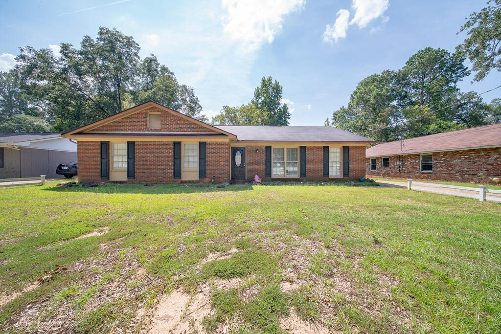 Single-story brick ranch with dark shutters and a broad front lawn.