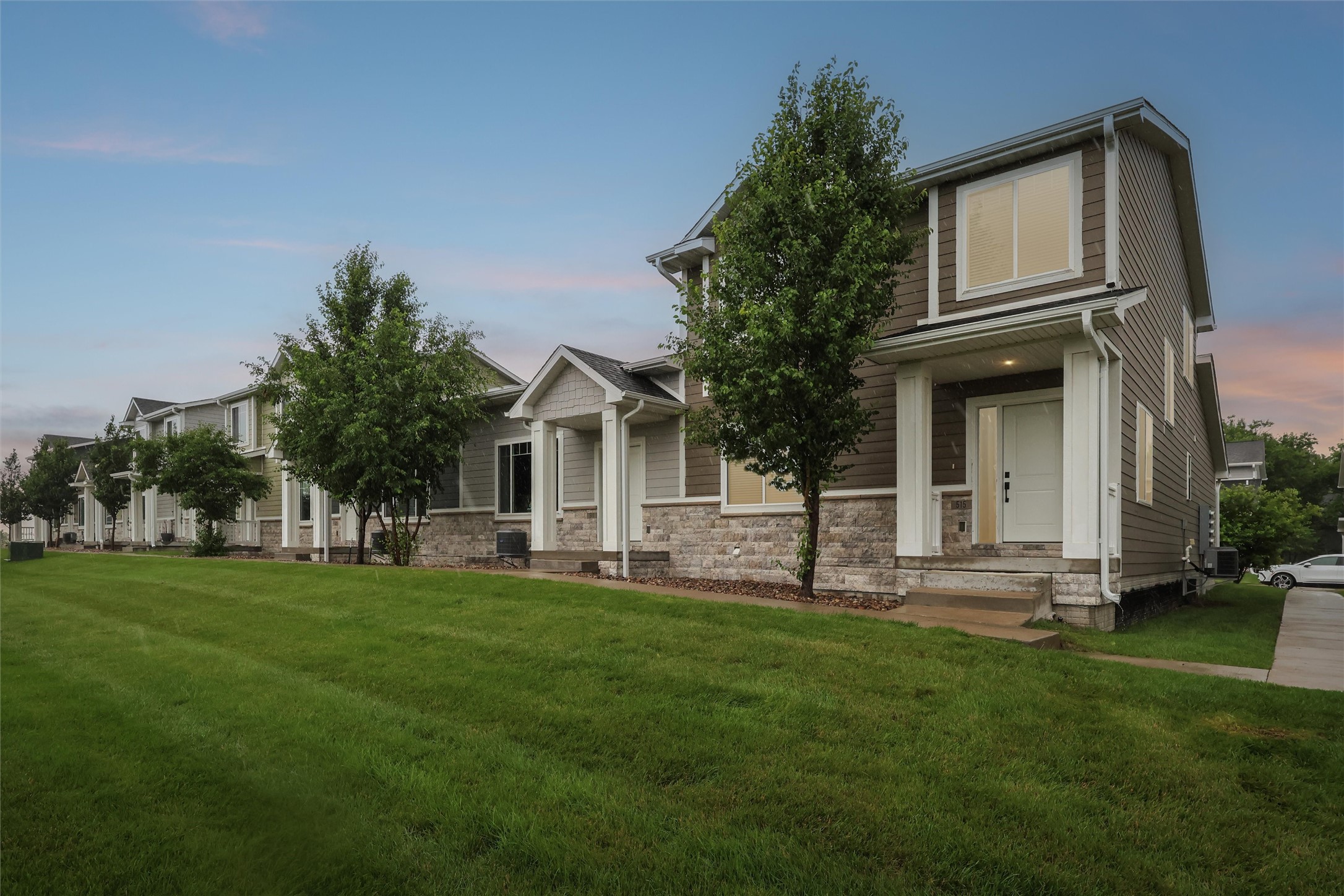 Two-story brown-sided home with white trim and stone veneer, numbered 516, beside a row of attached homes.