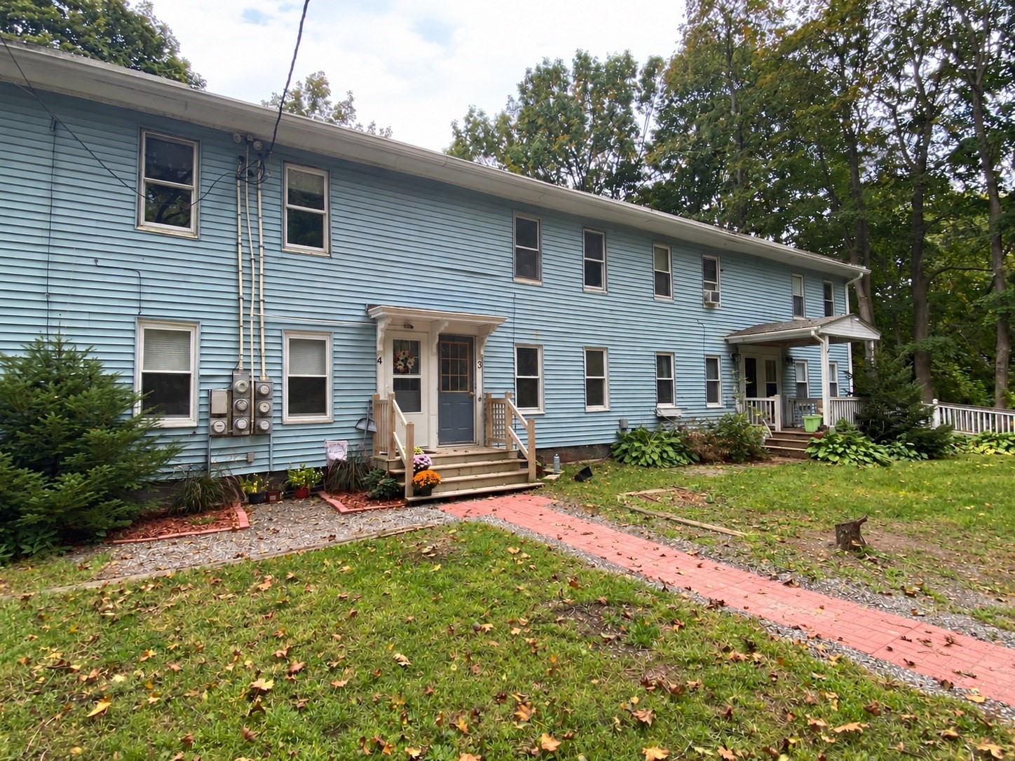 Two-story blue-sided residential building with multiple porches and a red brick walkway through the front yard.
