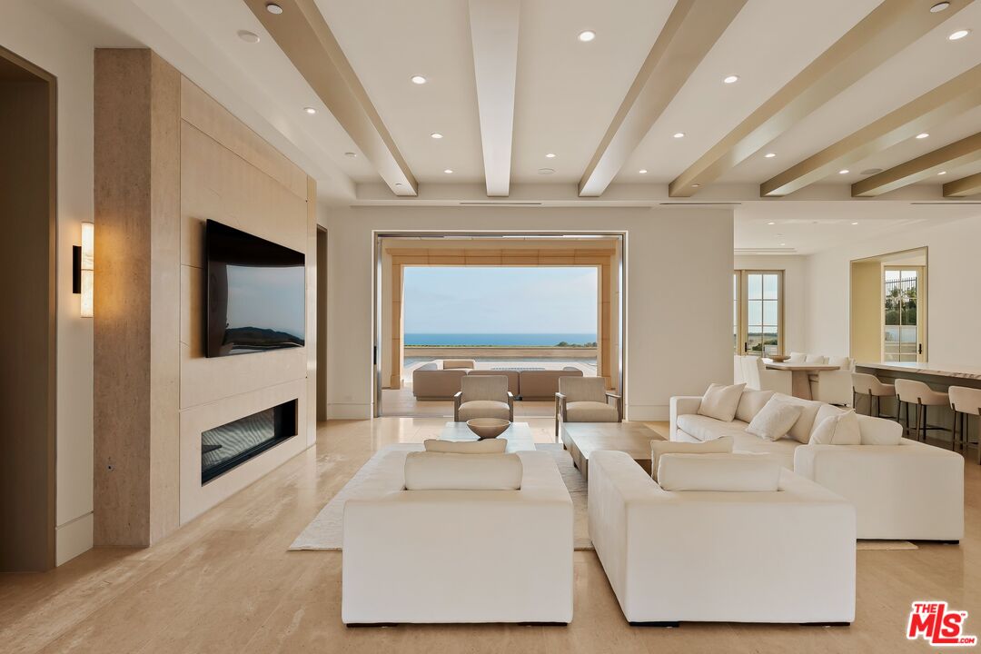 Living room with white sofas, a fireplace, and ocean views through a wide opening.