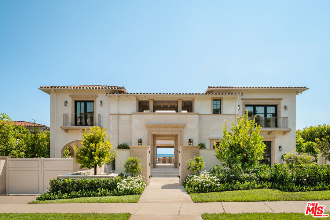 Two-story cream-stone home with upper balconies, a gated entry, and landscaped front walkway.