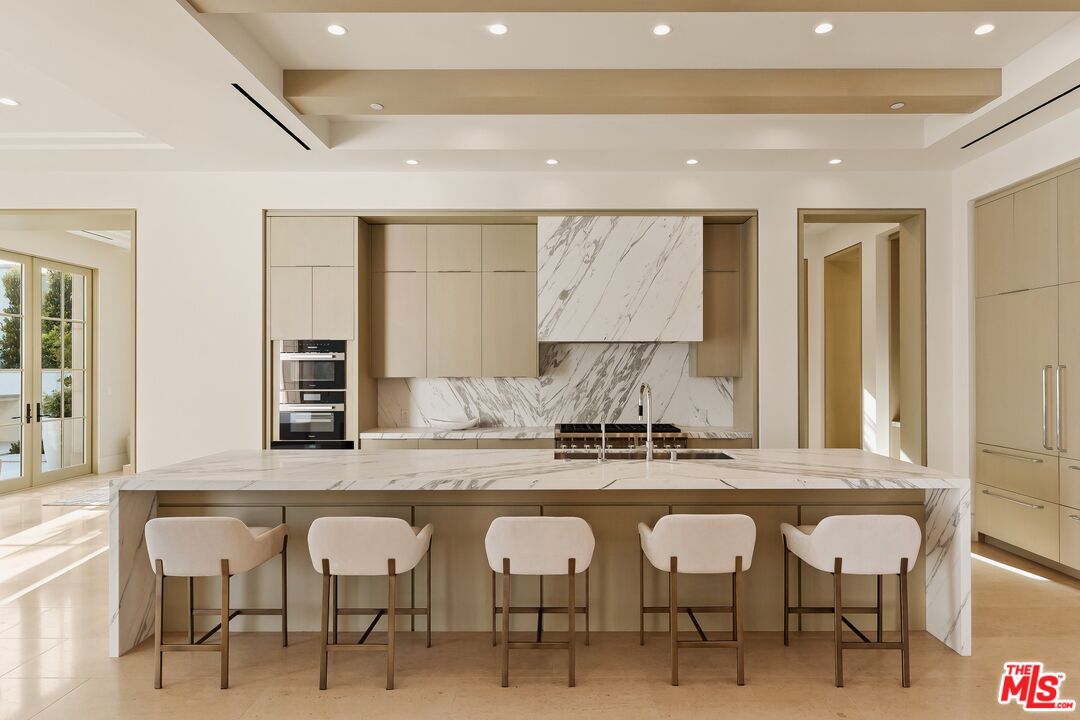 Modern kitchen with a veined marble island, five bar stools, and beige cabinetry