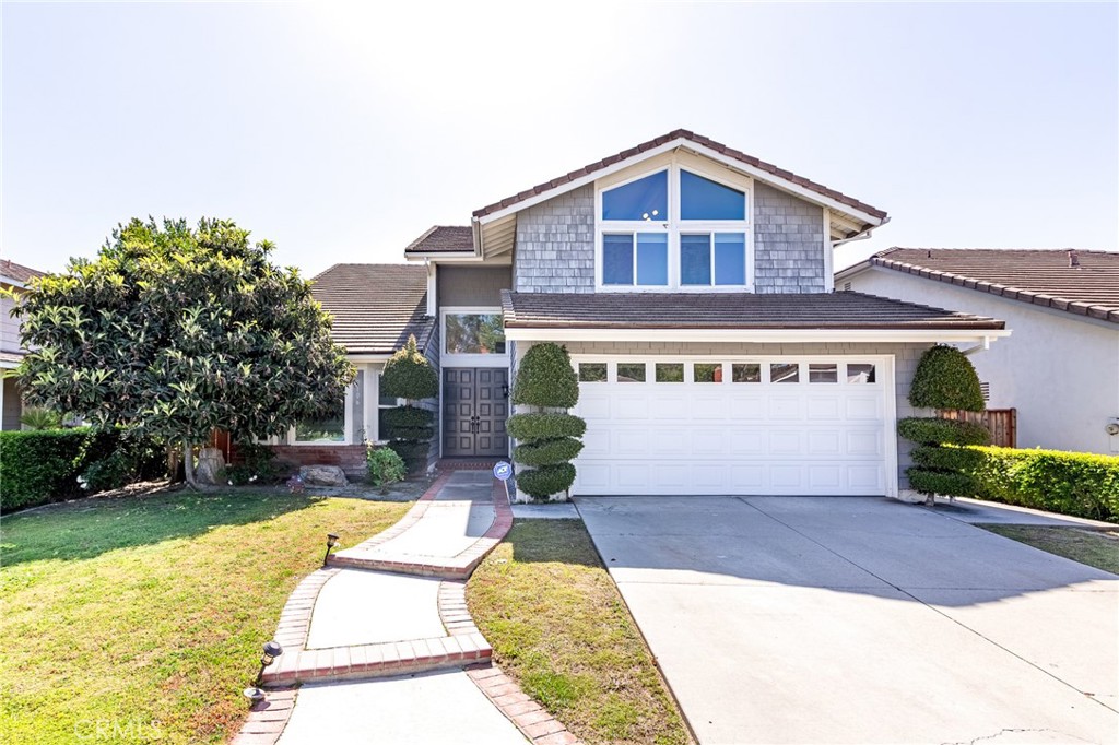 Two-story house with gray shingle siding, a white garage door, and a curved walkway through the front lawn.