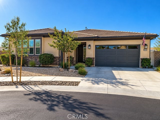 Single-story stucco home with a dark double garage door, desert landscaping, and an American flag by the entrance.