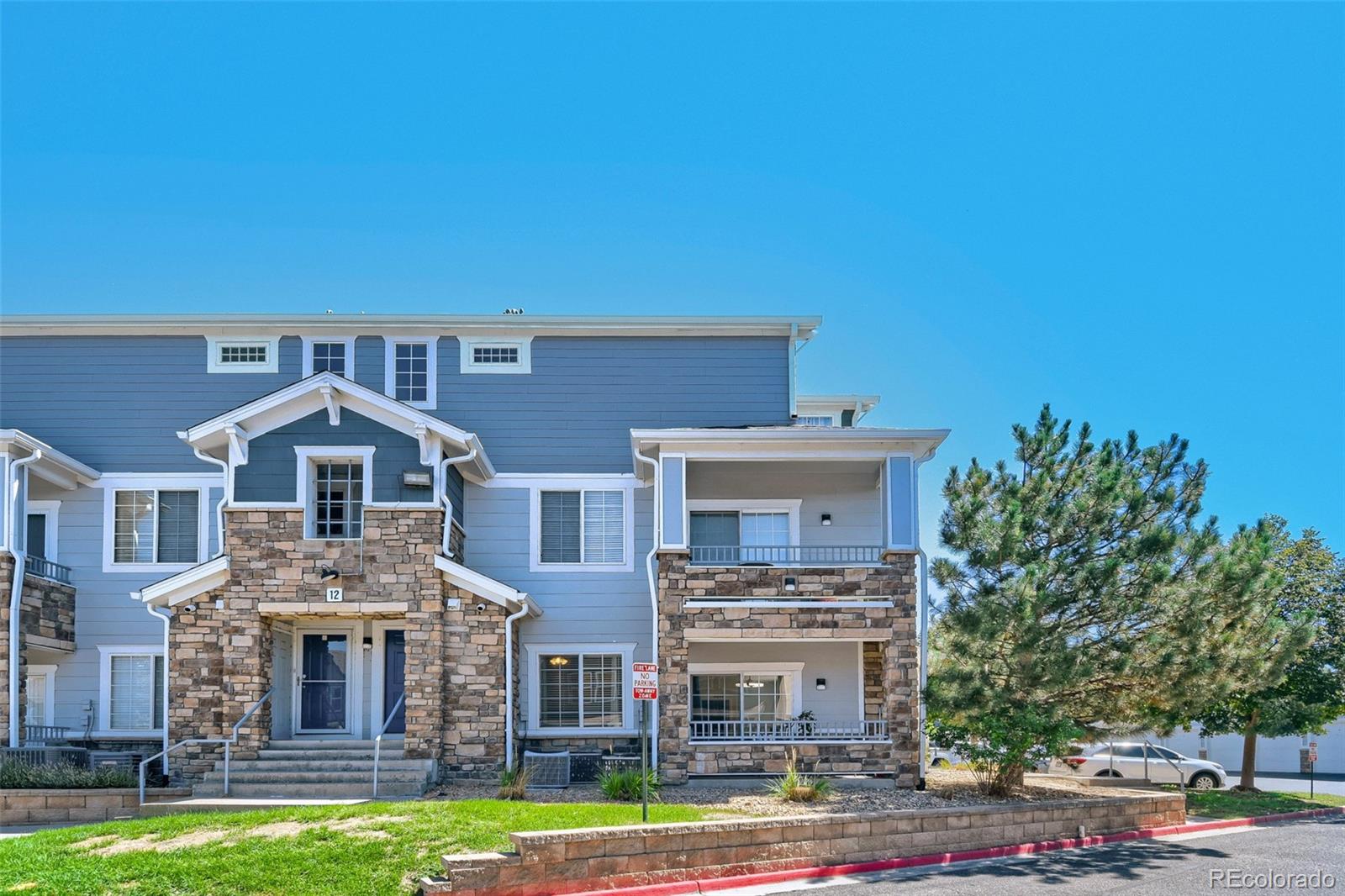 Blue condominium building with stone accents, balconies, and a central entrance.
