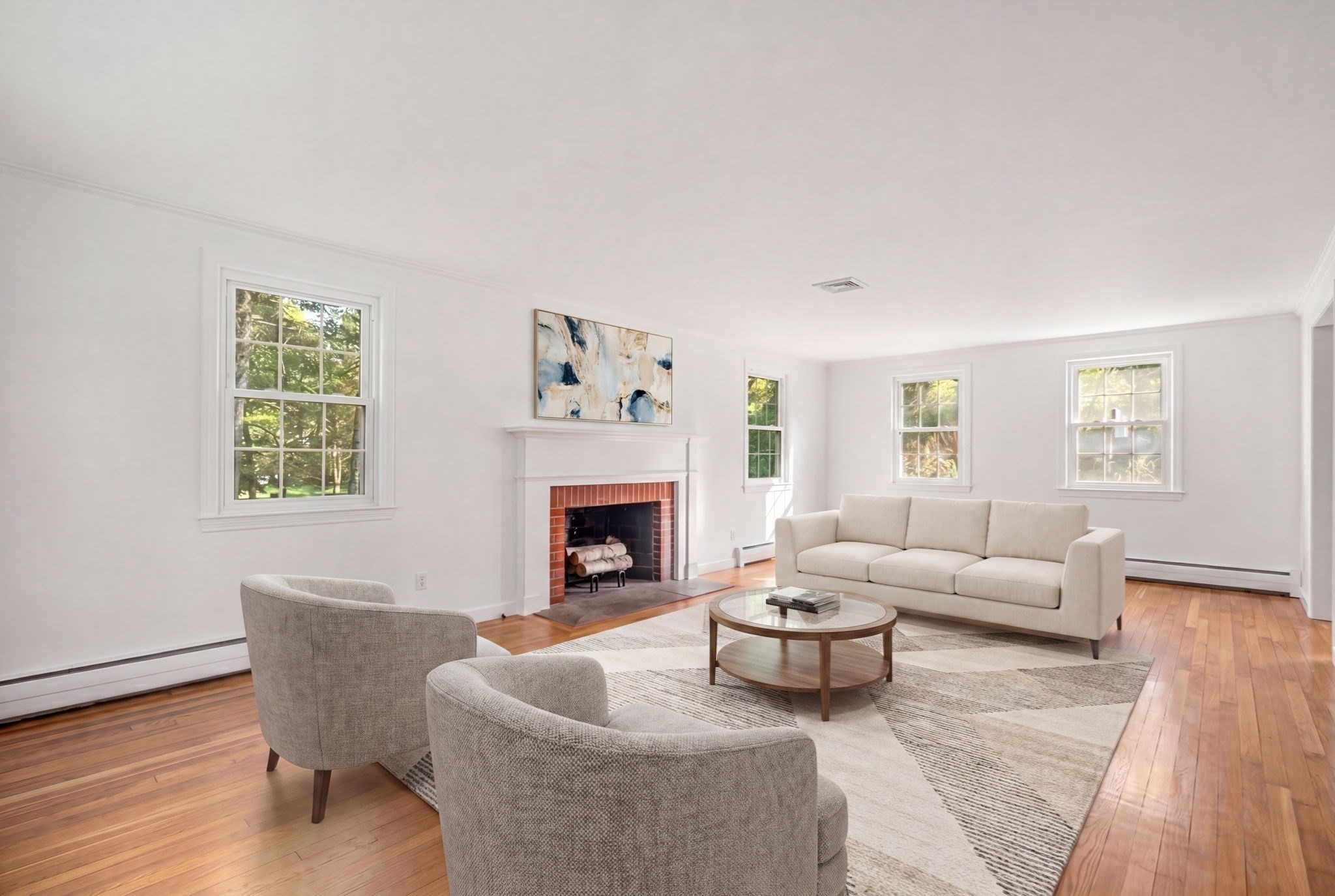 Staged living room with a brick fireplace, hardwood floors, and large windows.
