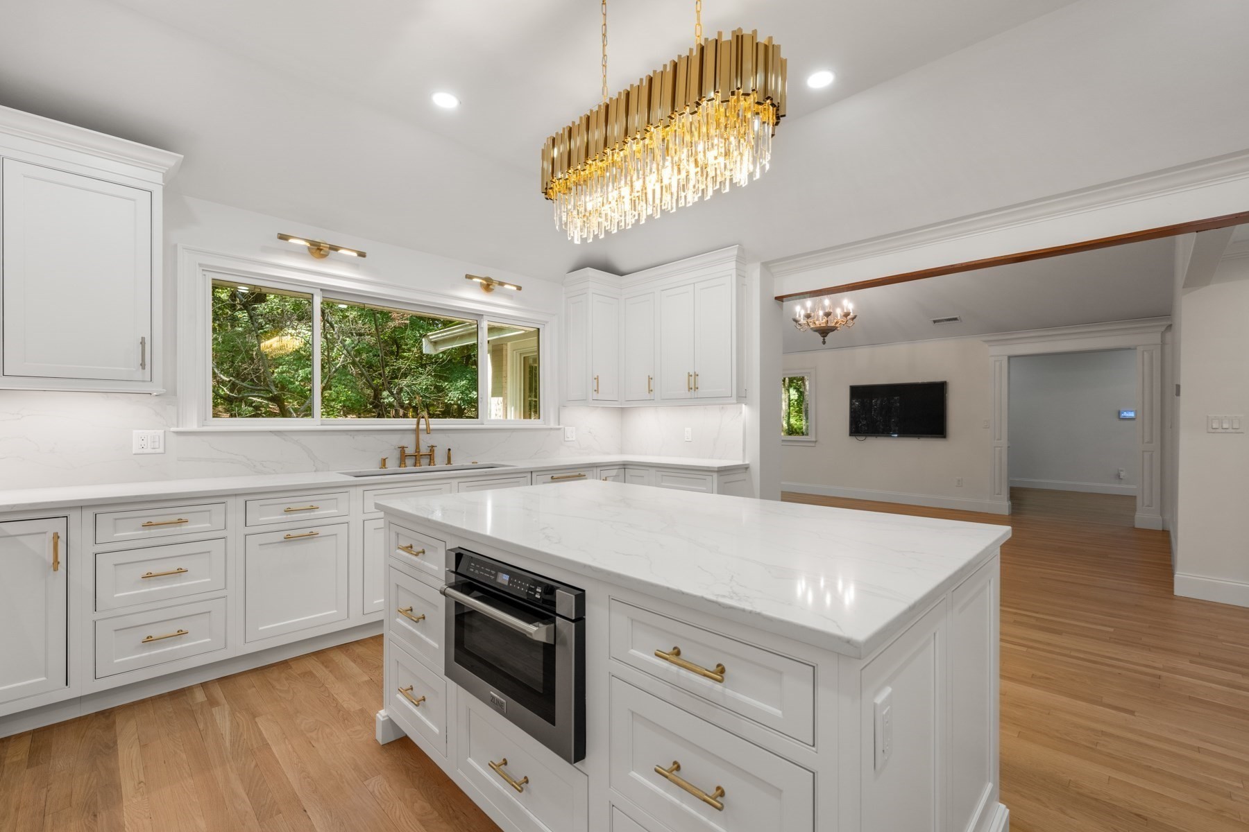 White kitchen with a large island, brass fixtures, and a gold crystal chandelier.