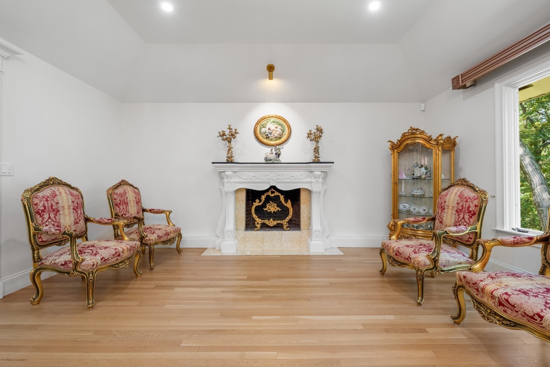 Sitting room with an ornate white fireplace and red-and-gold chairs.
