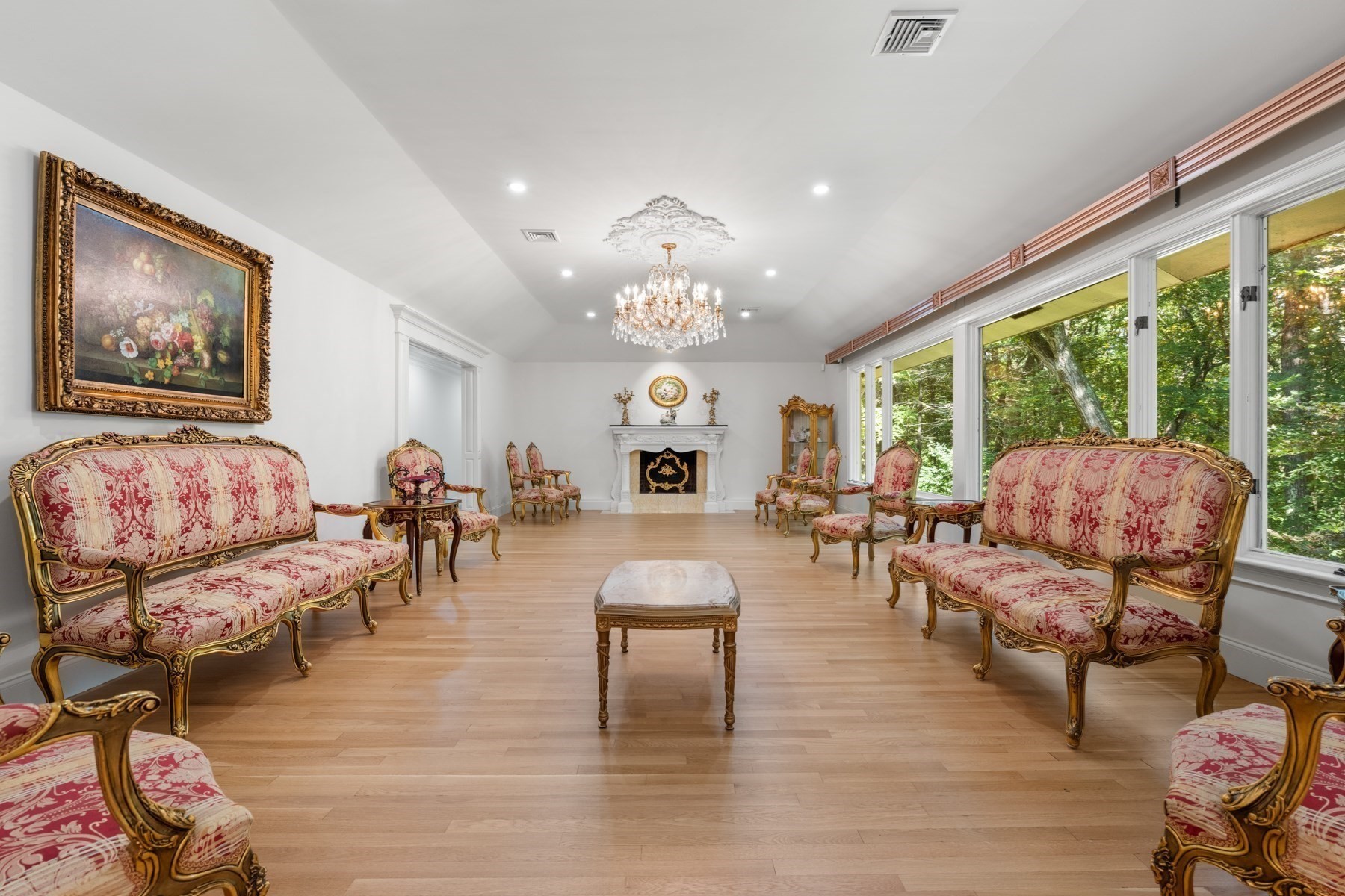 Formal living room with ornate red-and-gold seating, a crystal chandelier, white fireplace, and large windows.